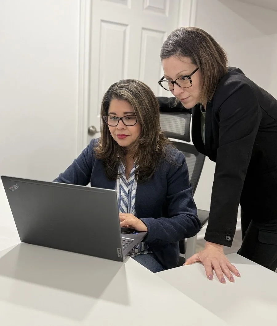Ana María Domínguez, sentada frente al computador, y Zaira Rodríguez, de pie a su lado